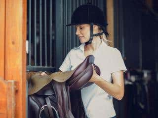 A woman is putting her saddle away after a ride.