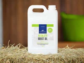 Horseland Vitality Boost Oil sitting on top of a bale of hay