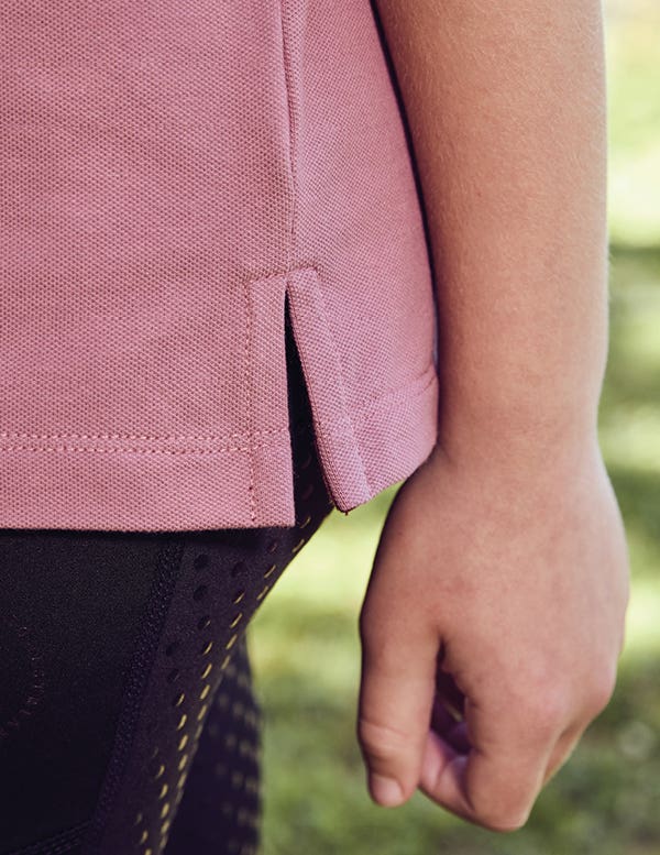 Close up of side seam of Dublin Kids Cotton Plique Short Sleeve Polo standing in front of arena gate