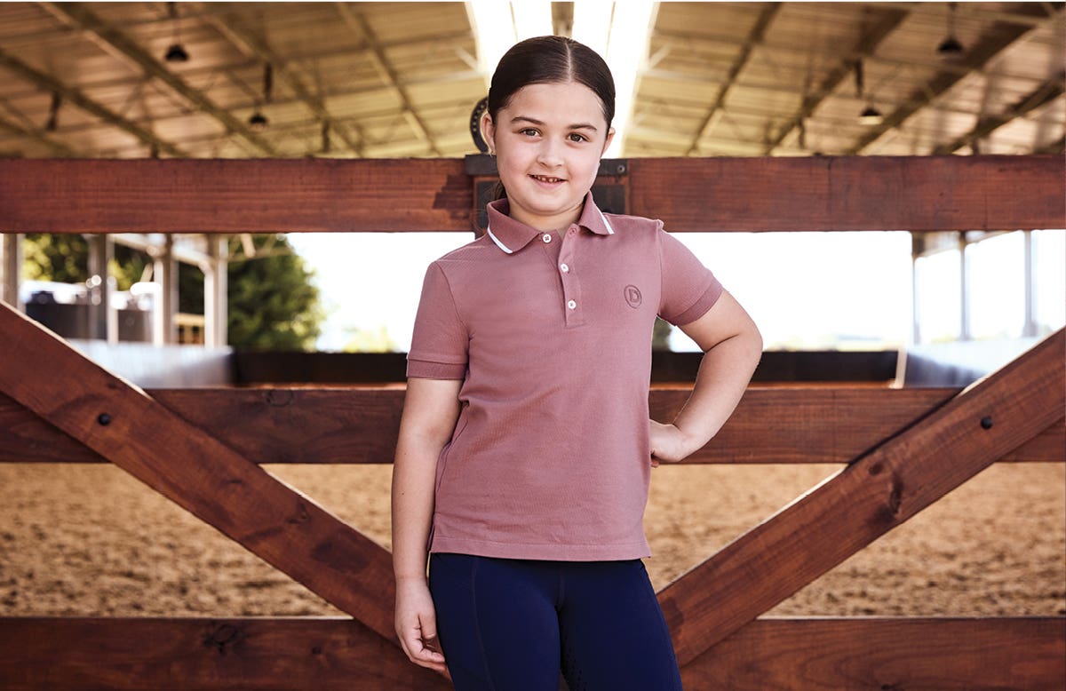 Young girl wearing Dublin Kids Cotton Plique Short Sleeve Polo standing in front of arena gate