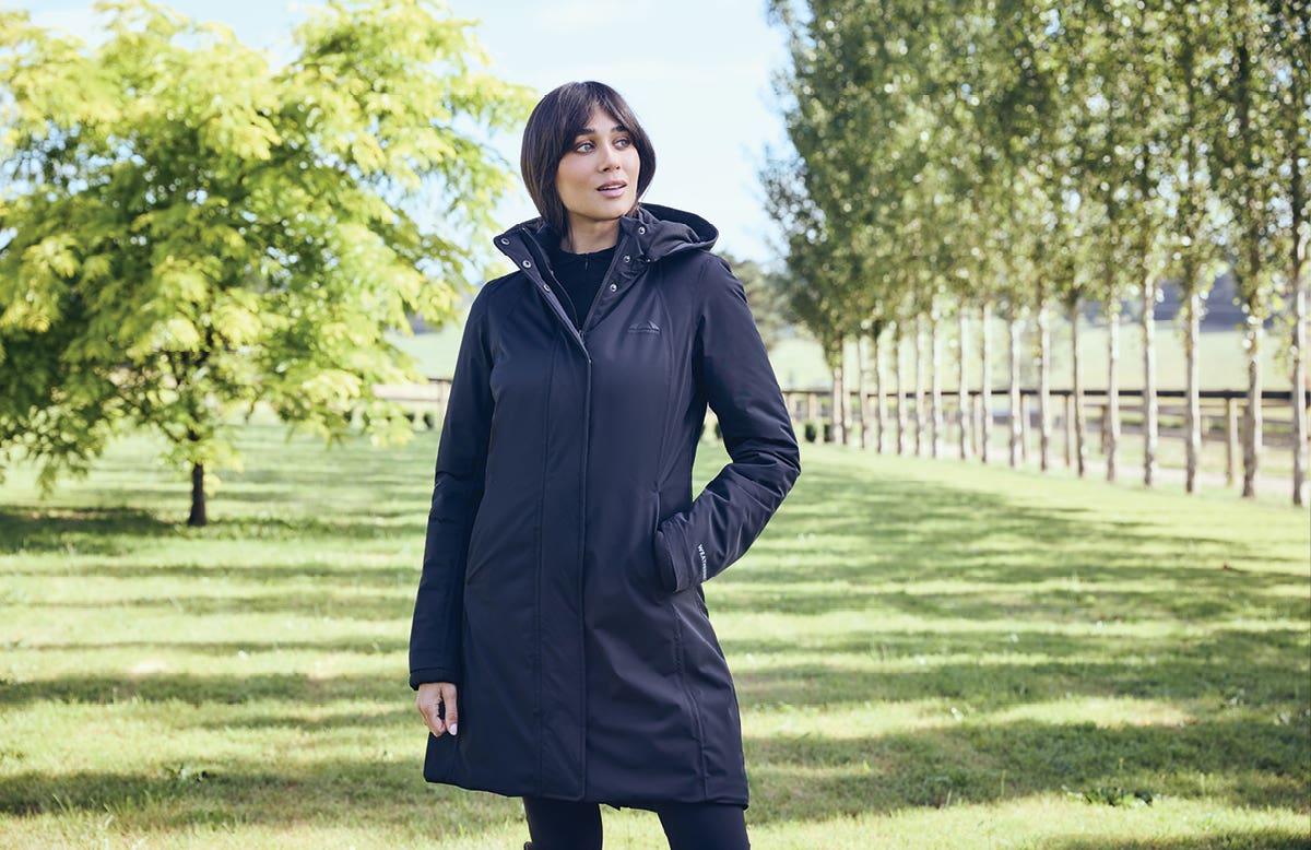 Model standing in a field wearing WeatherBeeta All Purpose Longline Waterproof Equestrian Jacket