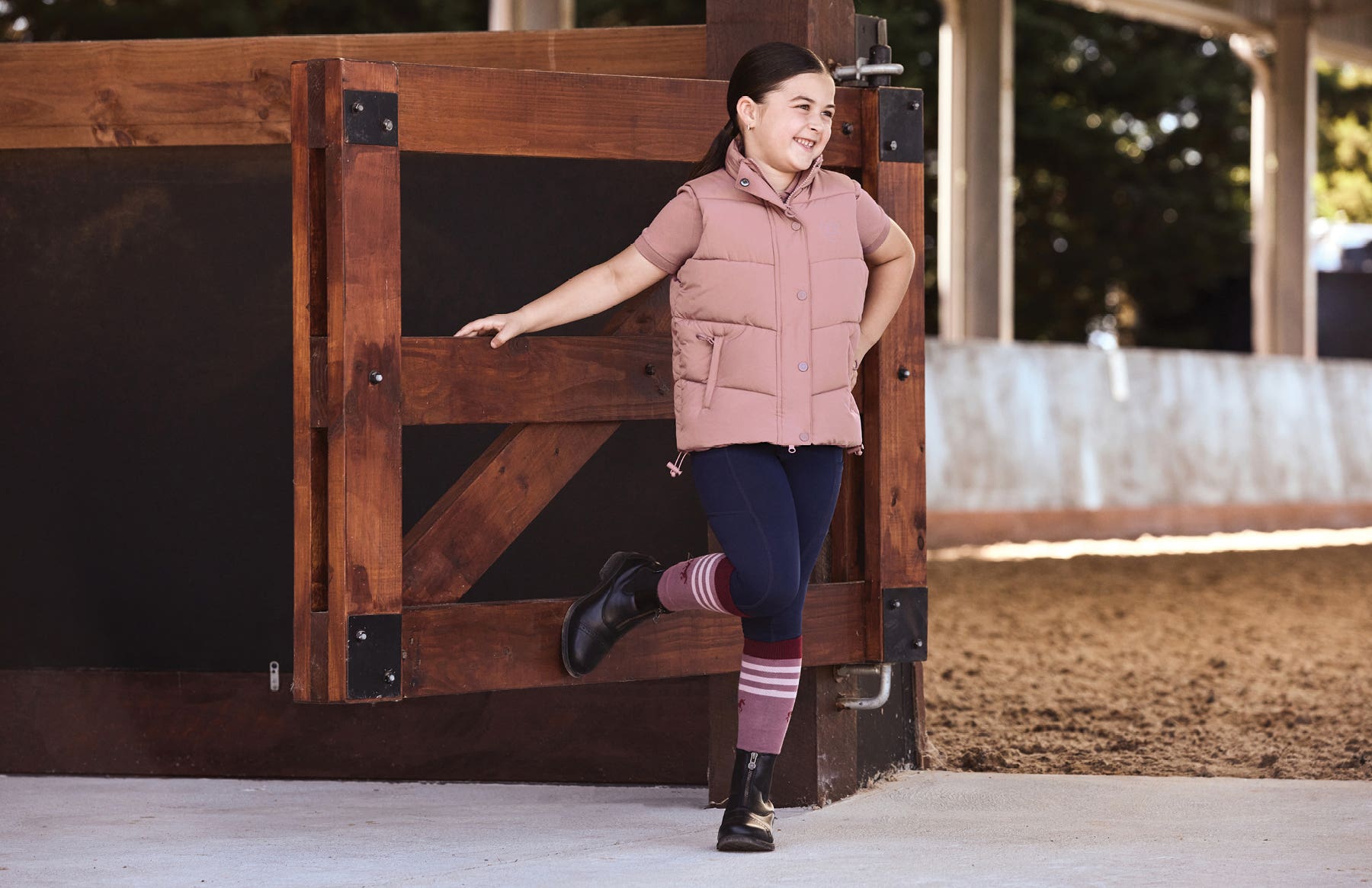 Young girl standing against arena gate wearing Dublin Kids Clothing