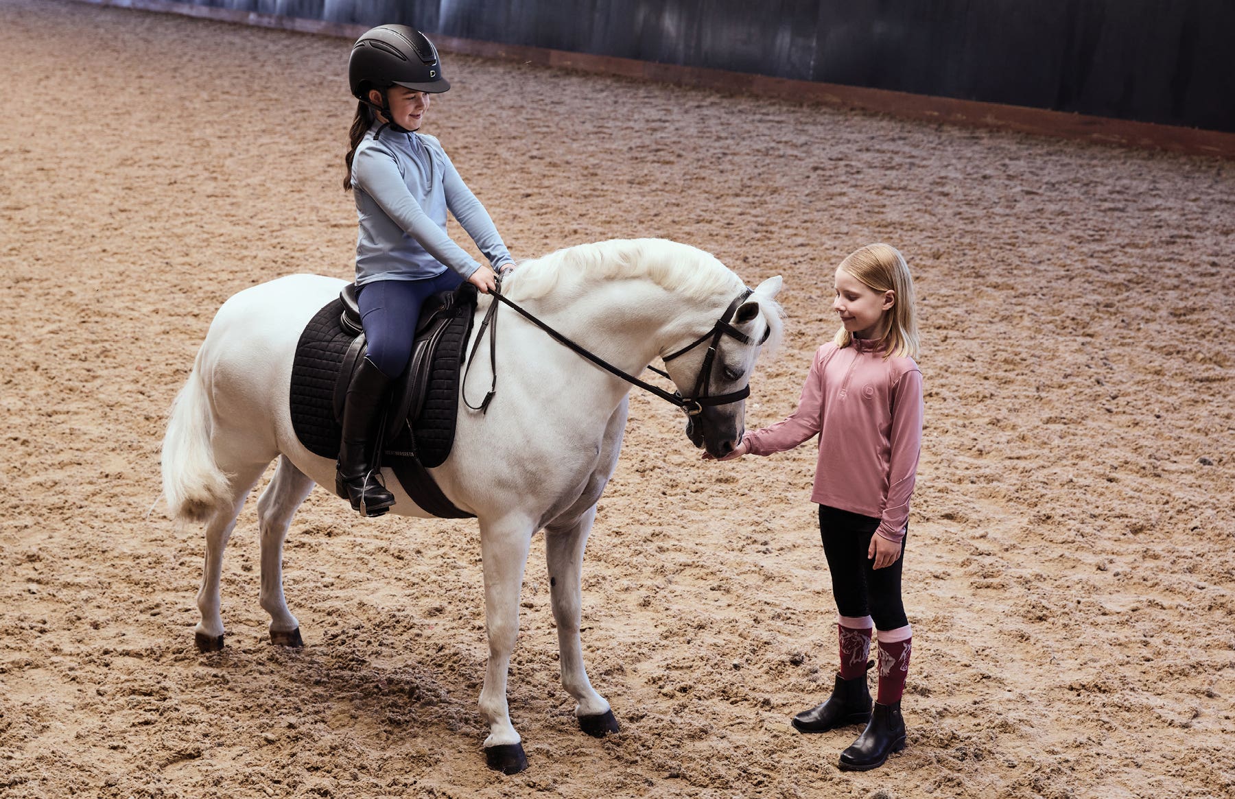 Two children wearing Dublin clothing in arena with grey pony