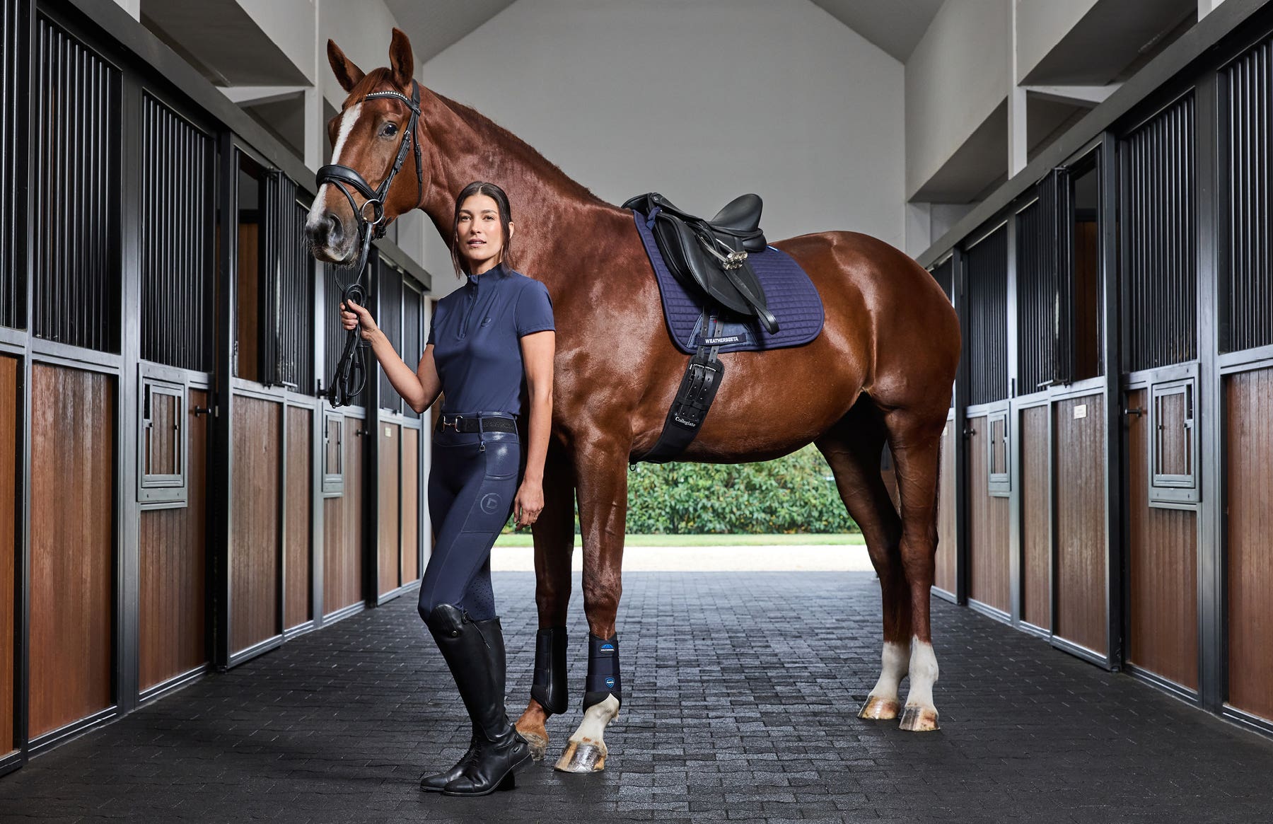 Model wearing Dublin clothing standing in stables holding horse